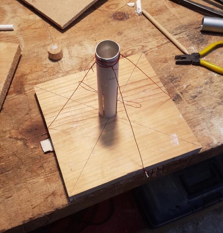 Improvised compression test rig: a metal cylinder held vertical by four guide wires on a wooden board